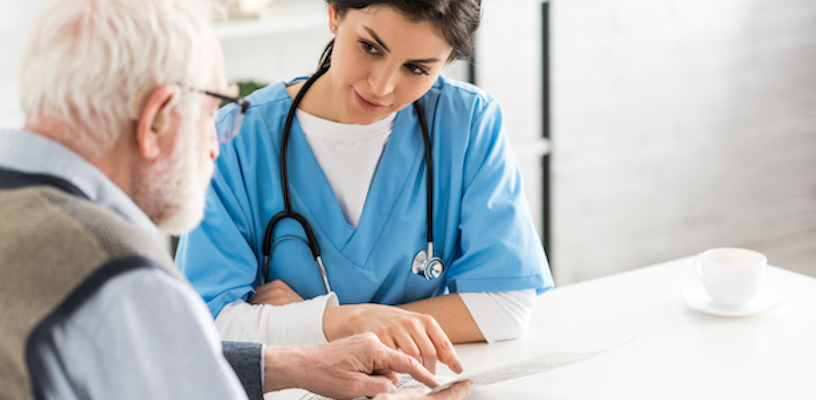 A woman wearing scrubs and a stethoscope helps an older man with paperwork